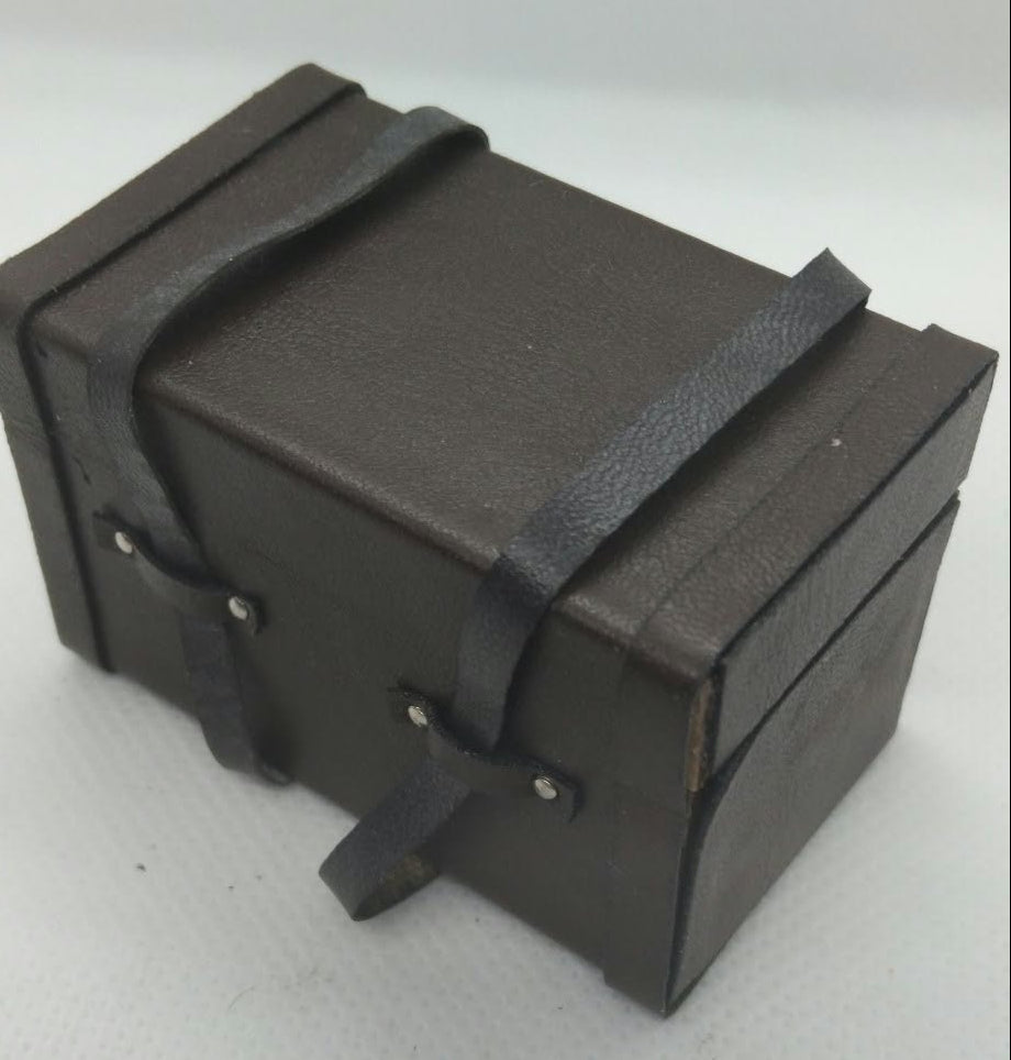 A miniature dark brown faux-leather storage box with black straps and silver rivets, photographed on a light gray background.