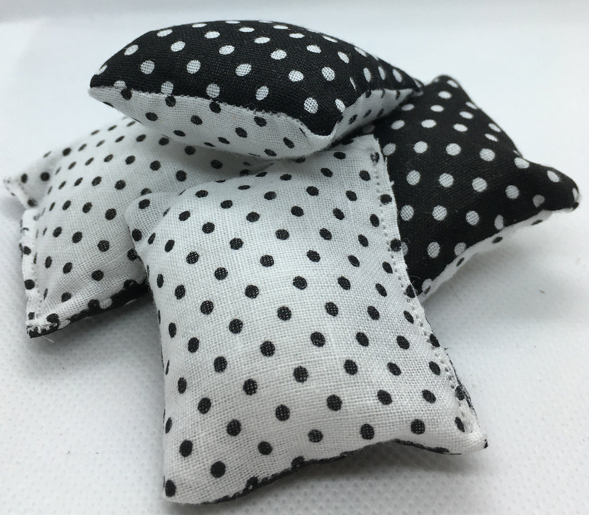 Three small fabric square pillows with black and white polka dot patterns, arranged on a white textured surface against a white background.