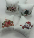 Four small white decorative pillows with embroidered Christmas designs, including a hot cocoa mug, a Christmas tree, berries, and a snowman, arranged on a white textured fabric background.