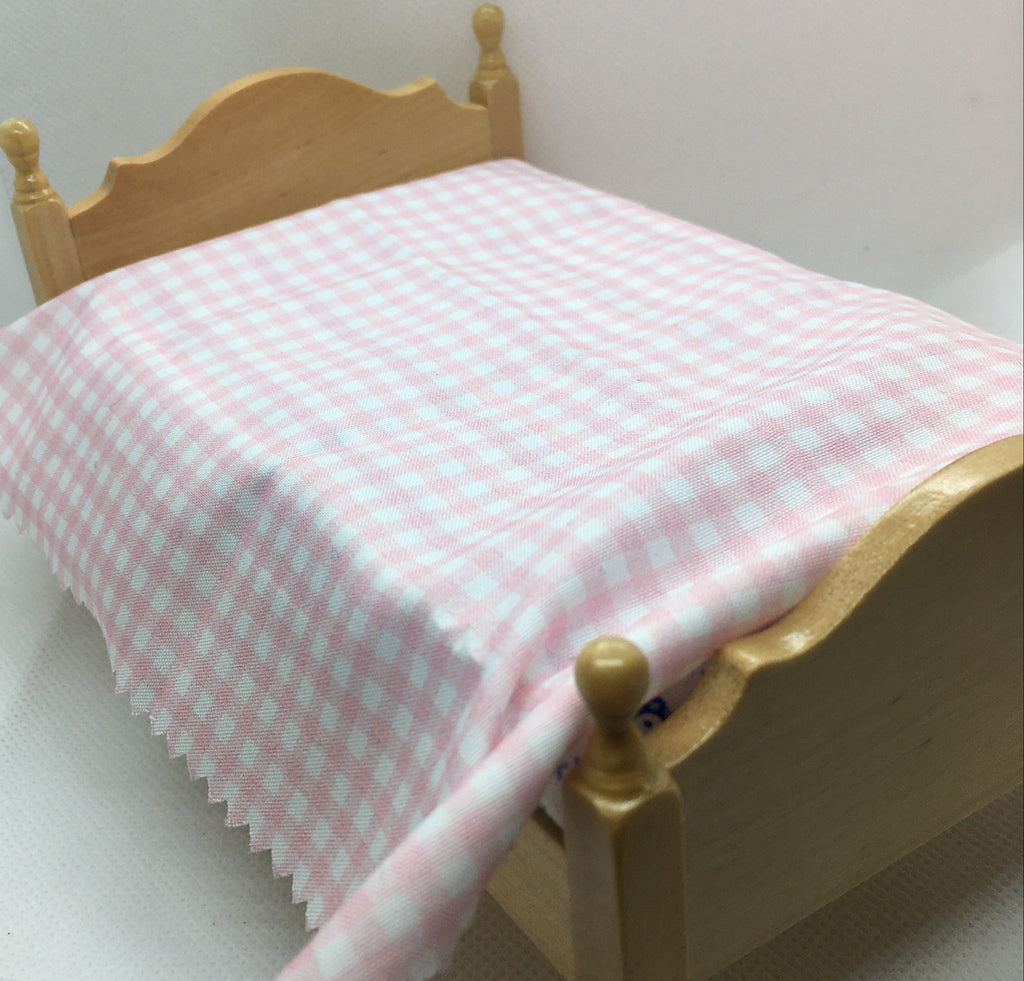 A miniature dollhouse bed made of light natural wood, styled with a pink and white gingham checkered blanket.