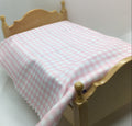 A miniature dollhouse bed made of light natural wood, styled with a pink and white gingham checkered blanket.