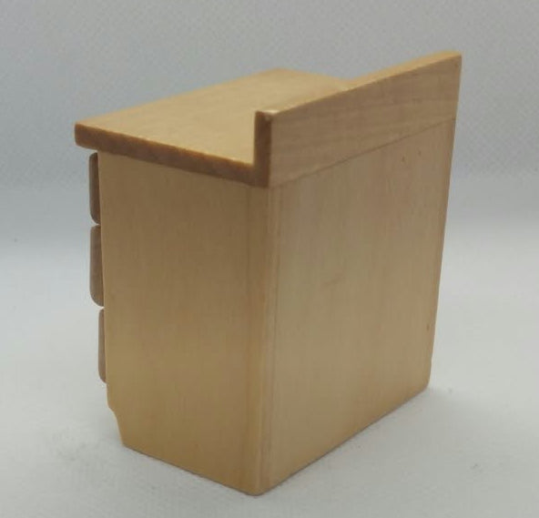 A small light wood back of a  miniature cabinet- with a slanted top, photographed on a white surface .