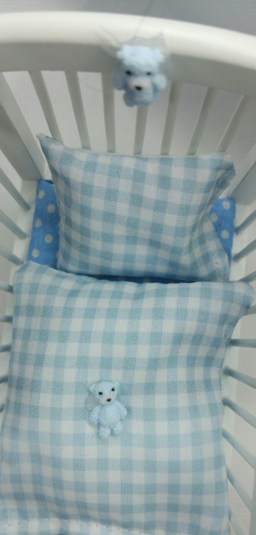 Light blue and white gingham baby pillow set with a matching crib and a small teddy bear motif,.