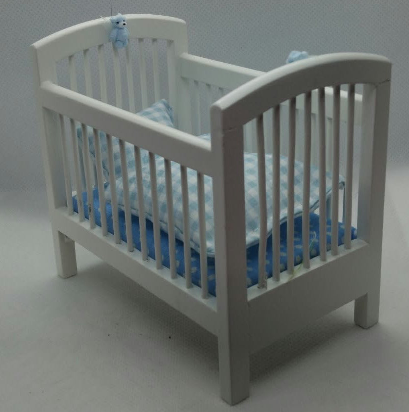 A miniature white wooden baby crib with a blue and white striped mattress and bedding, shown on a light gray studio background.
