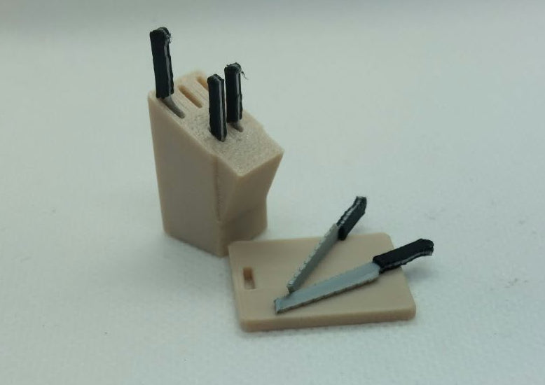 A miniature dolls house  kitchen knife block set with beige plastic blocks and black plastic knife handles, displayed on a white surface.
