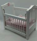 A miniature white dollhouse crib with pink bedding and a pink bunny ornament, shown on a plain white surface.