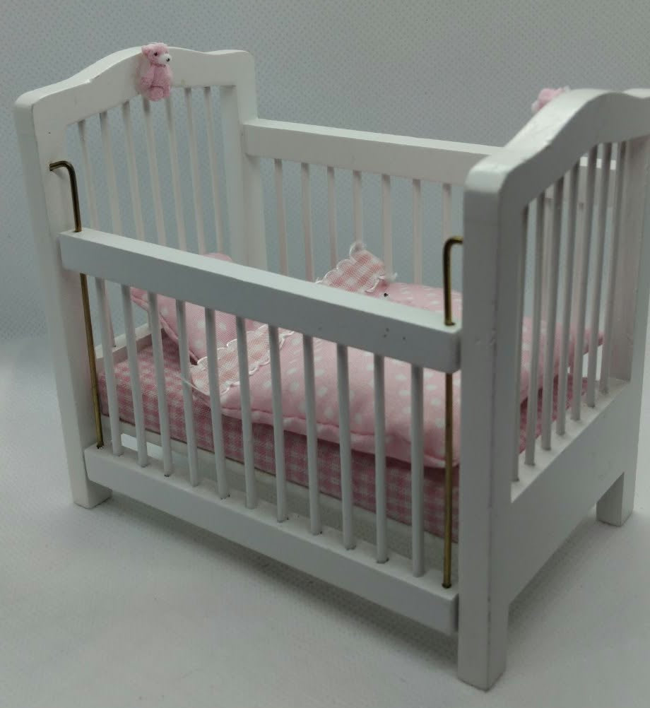 A miniature white dollhouse crib with pink bedding and a pink bunny ornament, shown on a plain white surface.