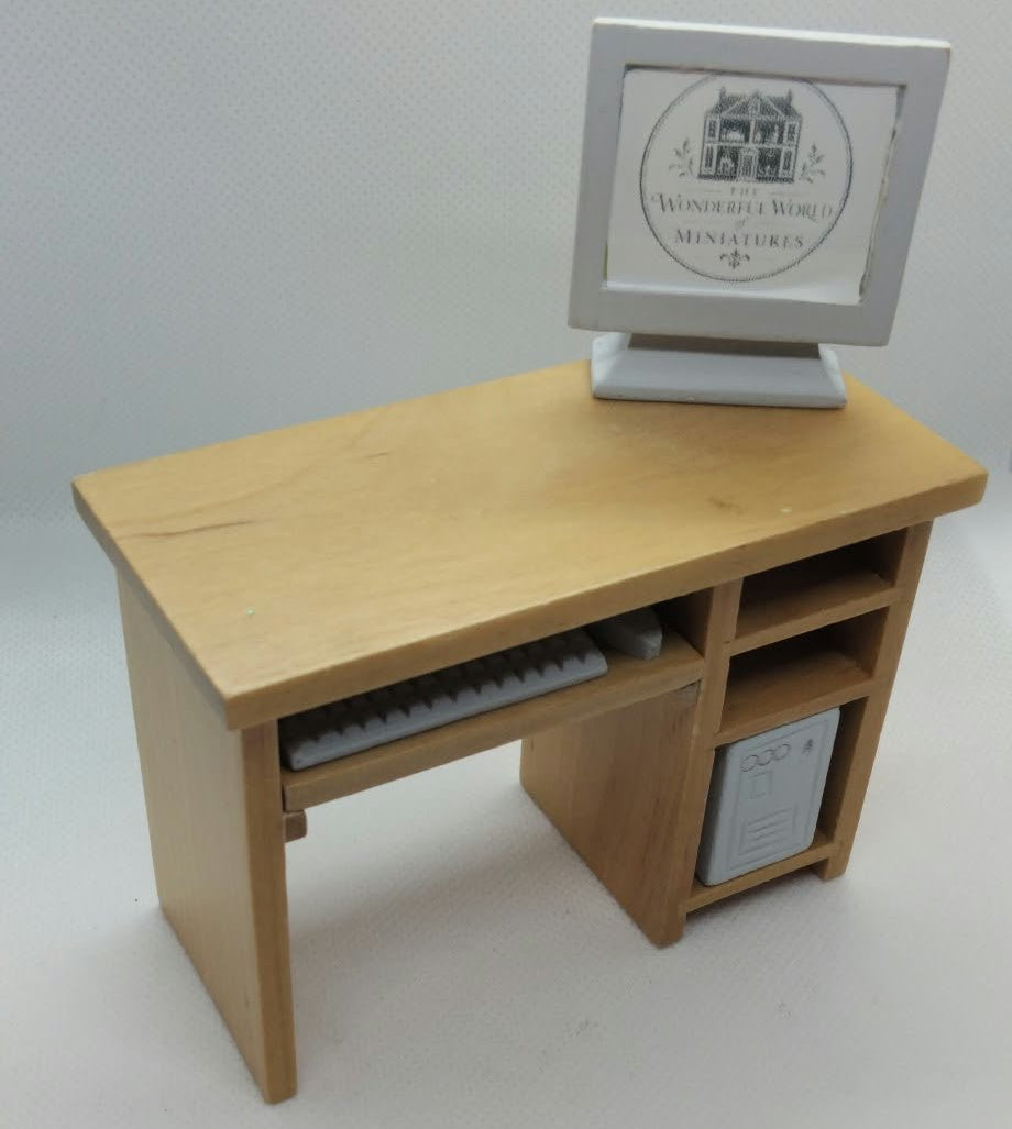 A miniature wooden desk with a computer monitor and keyboard, photographed on a white studio background.