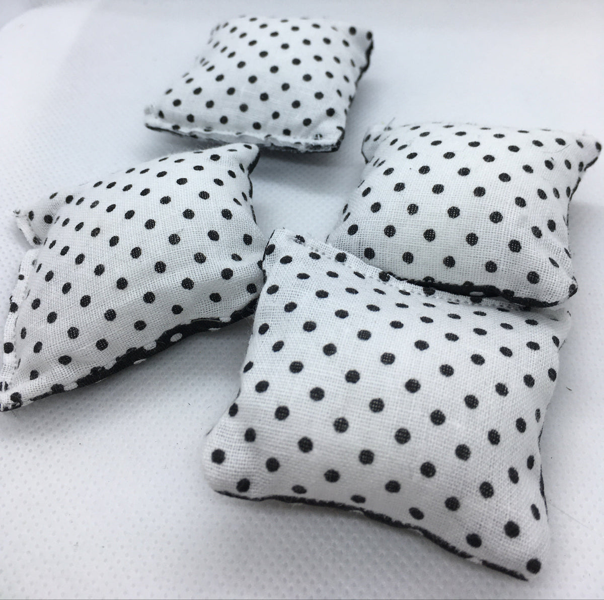 Four small square white fabric pillows with black polka dots, arranged on a white textured surface.