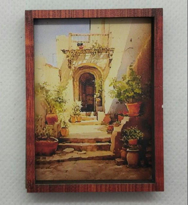A small rectangular framed picture with a reddish-brown wooden frame, mounted on a textured white wall. The print depicts a warm-toned architectural courtyard scene.