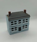 A miniature model of a two-story house, featuring a light blue body, a dark gray roof, and brown chimney pots, set against a plain light gray background.