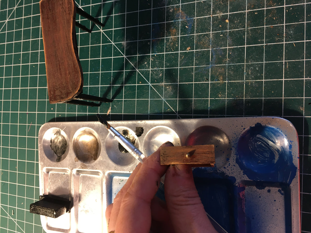 this shows a hand holding one of the table drawers and a paint brush and paint with the table in the background on a cutting matt.
