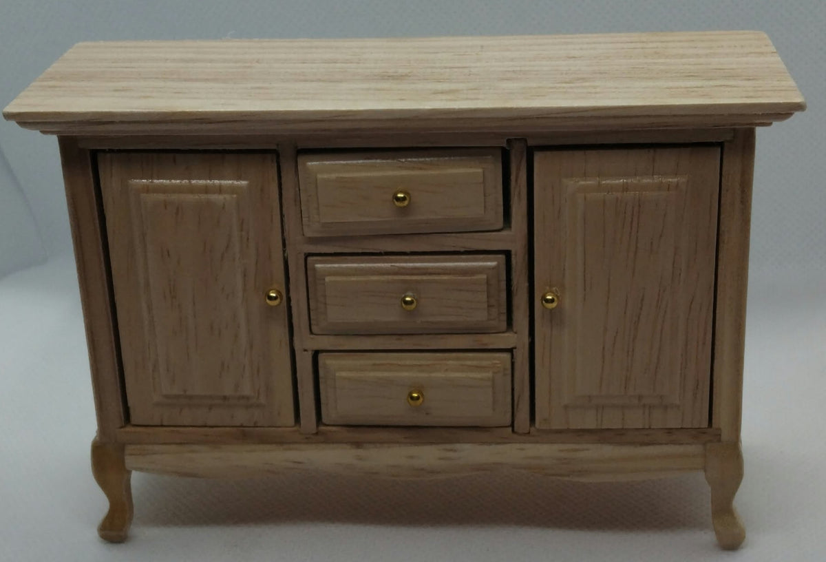 A miniature wooden sideboard cabinet with three drawers and two doors, featuring a light oak wood grain finish and small brass-colored knobs, photographed against a neutral gray background.