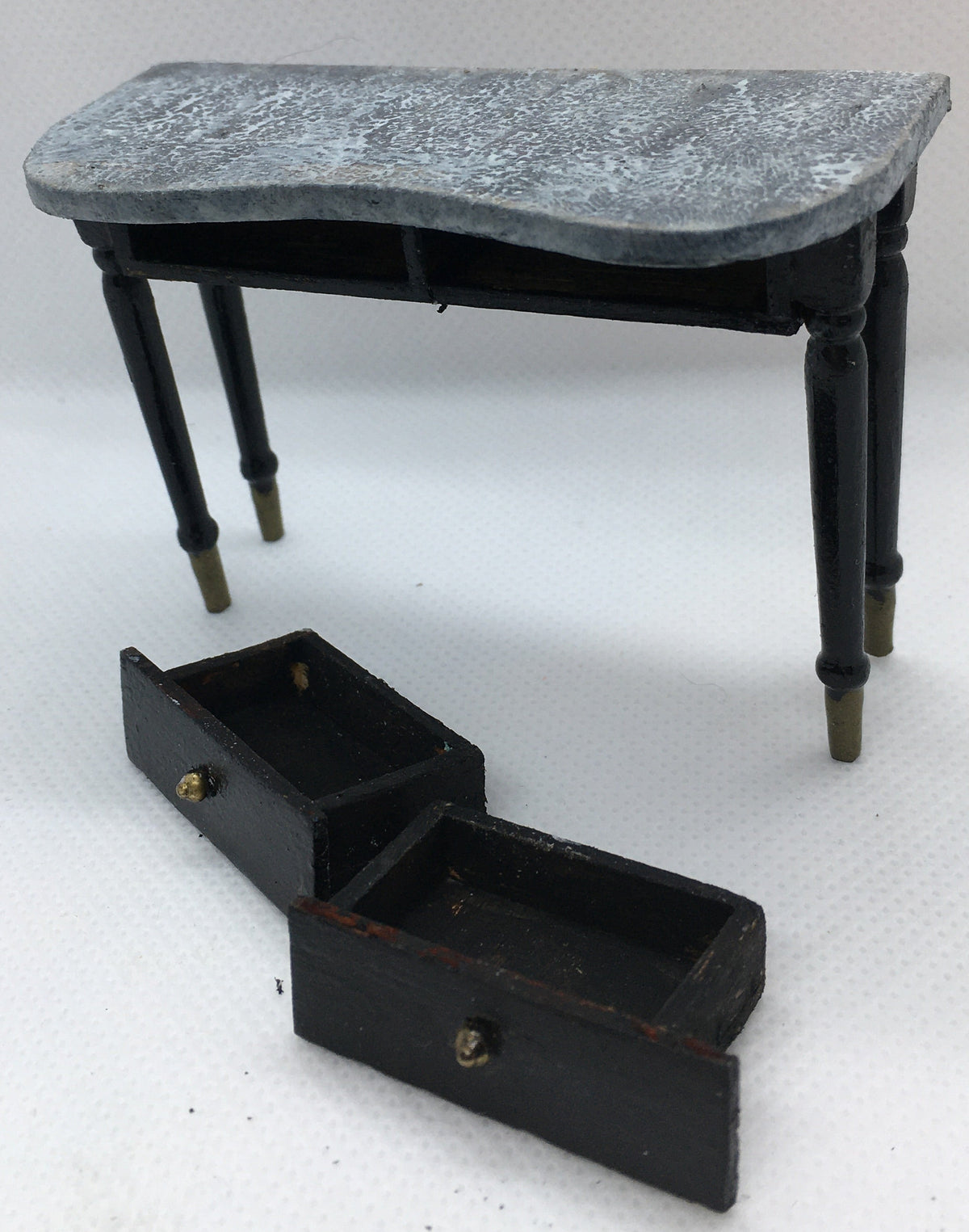 A miniature black console table with a gray marble-patterned top and two open drawers, photographed on a white textured background.